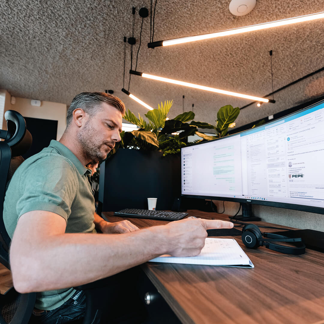 Medewerker op kantoor werkt met dubbele schermen en beheert e-mails en werkzaamheden